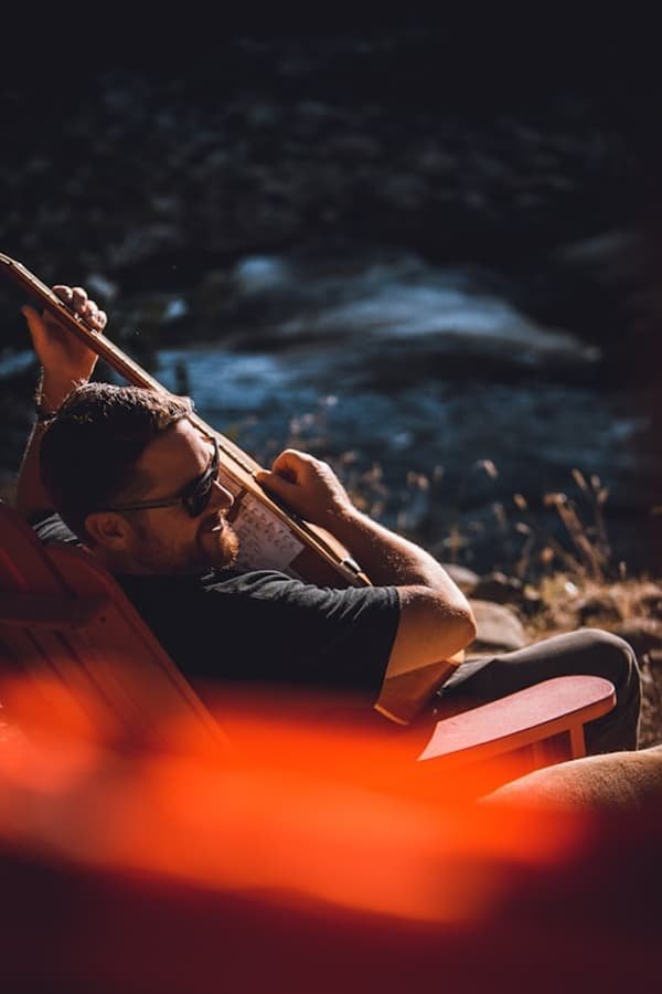 A-man-blaying-guitar-on-an-orange-chair-outside-by-Nick-Rickert-on-Unsplash